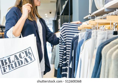 Side View Of A Woman Looking Through Clothing Rack And Holding Black Friday Bag 