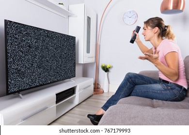 Side View Of A Woman On Sofa Frustrated With A TV Screen Glitch