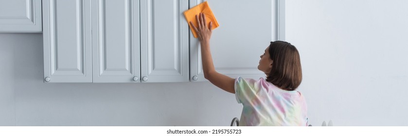 Side View Of Woman With Rag Cleaning Cupboard In Kitchen, Banner