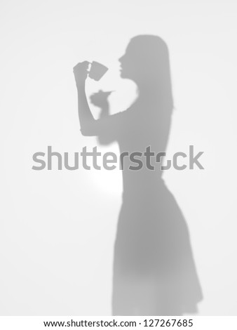 side view of woman silhouette drinking a cup of coffee behind a diffuse surface