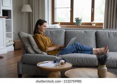 Side view woman sits on sofa in living room put laptop on laps enjoy online chat, share messages in social media, communicates remotely use internet. Modern tech, fun, leisure or telecommuting concept - Powered by Shutterstock