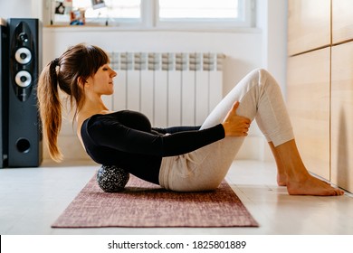 Side view of woman in sportswear using duoball for myofascial release exercise for spine lying on yoga mat at home or office, overcome pain, rehabilitation concept.