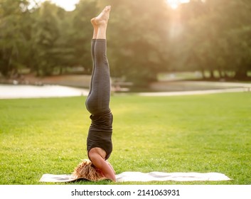 Side View Of Woman Standing In Salamba Sirsasana Position - Athlete Exercising Outdoors In Park At Sunset - Supported Headstand Posture With Straight Legs