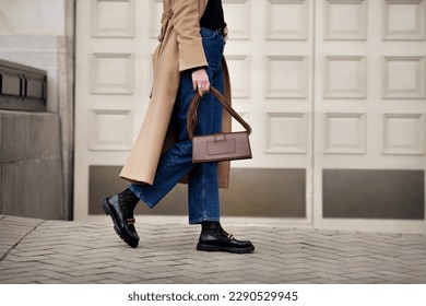 Side view woman walking street in fashionable spring or autumn clothes cashmere coat, jeans, black loafers shoes and handbag. Female model in motion, street style fashion, close up legs - Shutterstock ID 2290529945