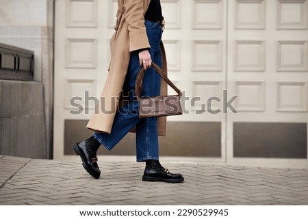 Side view woman walking street in fashionable spring or autumn clothes cashmere coat, jeans, black loafers shoes and handbag. Female model in motion, street style fashion, close up legs