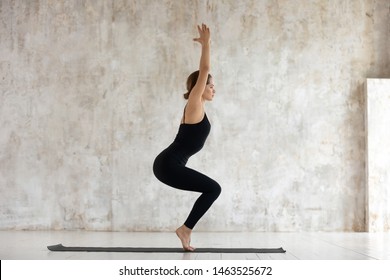 Side View Woman Wears Black Sportswear Performs Exercise Do Low Squatting Chair Pose Utkatasana Yoga Against Beige Grunge Studio Wall, Asana Increases Flexibility Improve Overall Body Strength Concept