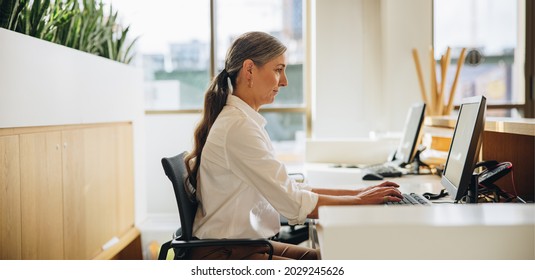 Side View Of Woman Working On Computer At Desk In Office. Female Executive Using Computer At Work