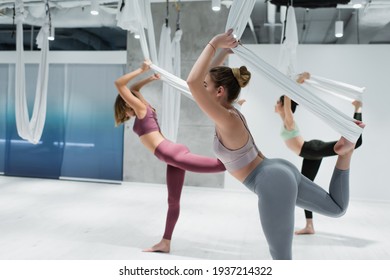 Side view of woman working out with straps near sportswomen on blurred background during fly yoga
