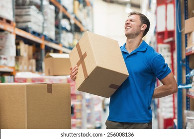 Side view of worker with backache while lifting box in the warehouse - Powered by Shutterstock