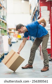 Side View Of Worker With Backache While Lifting Box In The Warehouse