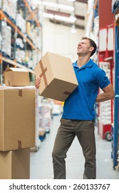 Side View Of Worker With Backache While Lifting Box In The Warehouse