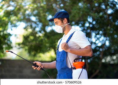 Side view of worker using crop sprayer in back yard