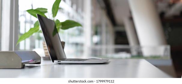Side view of worktable with laptop, office paper filing trays, decoration and copy space in modern office room