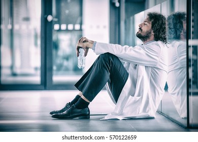 Side View Of Worried Doctor Sitting On Floor In Hospital