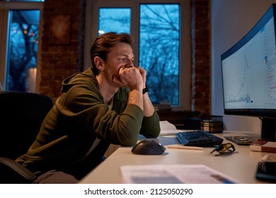 Side View Of Worried Male Trader Watching On Business Graph On Computer Monitor. Young Focused European Man Monitoring And Analyzing Stock Market Online At Home. Freelance And Remote Work