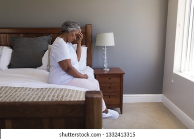 Side view of worried senior African American woman sitting on a bed at home - Powered by Shutterstock