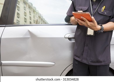 Side view of writing on tablet computer  while insurance agent examining car after accident