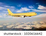 Side view of yellow aircraft in flight. The passenger plane flies high above the sunset clouds.