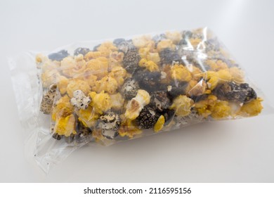 Side View Of Yellow And Black Colored Popcorn In A Clear Bag Isolated Against A White Background. Plastic Snack Bag Is Unopened.