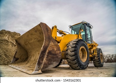 Side view of a yellow bulldozer with dirty metal bucket and black rubber wheels