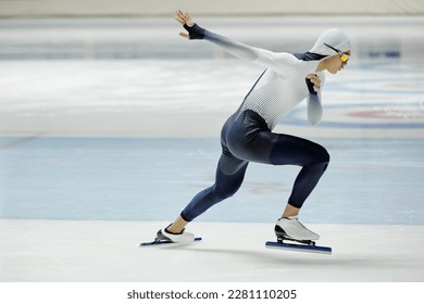 Side view of young active man in sports uniform and skates practicing exercises on ice rink while preparing for important competition