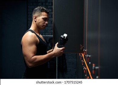 Side view of young adult athlete man standing in sport center at locker room, holding bottle with water and resting after training session - Powered by Shutterstock