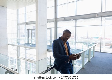 Side View Of Young African American Businessman Using A Tablet Computer Standing On A Mezzanine In The Atrium Of Bright Modern Business Building. Modern Corporate Start Up New Business Concept With