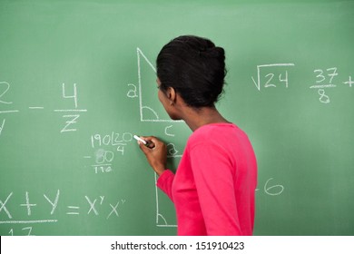 Side View Of Young African American Female Teacher Solving Mathematics On Board In Classroom