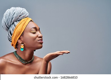 Side view of young african american girl posing isolated on grey background in studio. People sincere emotions lifestyle concept. Copy space. Blowing sending air kiss