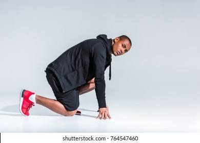 Side View Of Young African American Sportsman In Hoodie Ready To Run And Looking At Camera On Grey