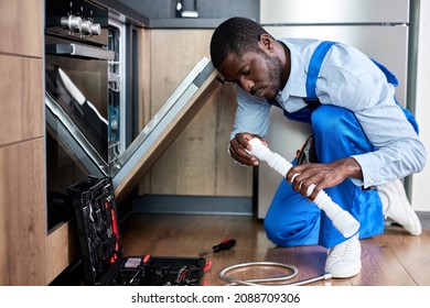 Side View Young African Handyman Repairing Dishwasher, Changing Siphon, Wearing Blue Workwear Overalls. Confident Professional Handyman Ar Home ,Focused On Work Alone, In Kitchen - Powered by Shutterstock