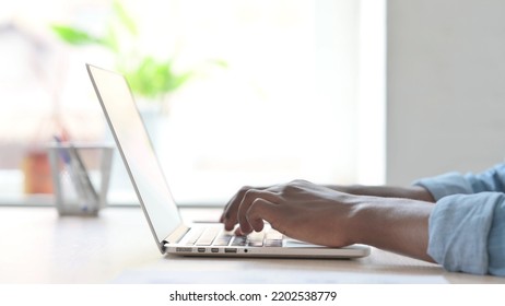 Side View Of Young African Man Typing On Laptop Keyboard