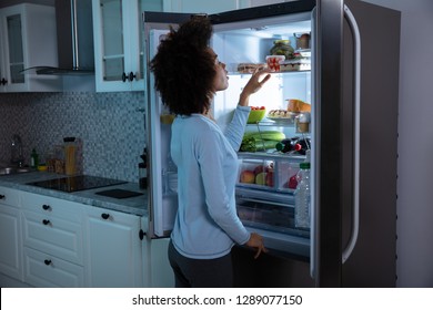 Side View Of Young African Woman Searching Food In An Open Refrigerator