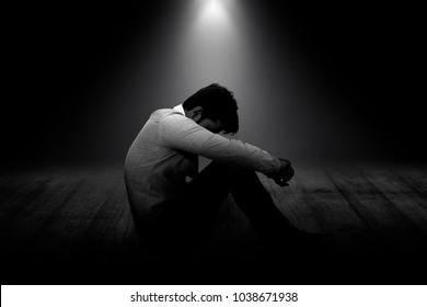 Side view of a young Asian formal man sitting disappointed on floor and looking down between legs. Grey scale black and white Background concept