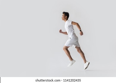 Side View Of Young Asian Male Athlete Running On Grey Background 