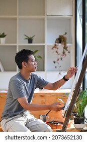 Side View Of Young Asian Man Painting On Canvas In Art Studio.