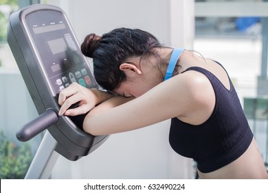 Side View Of Young Asian Woman Tired After Intense Workout On The Exercise Bike At The Gym. Relaxing Her Muscles After Workout In Fitness Club.