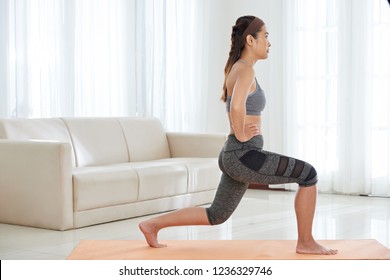 Side View Of Young Athletic Asian Woman In Activewear Doing Lunge Exercise While Having Workout At Home