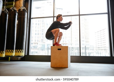 Side view of Young Athletic man which jumping on box in gym
