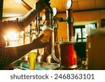 Side view of young bartender pouring beer while standing at the bar counter. Warm pub atmosphere. Concept of beer drink, alcohol, brewery, pub atmosphere, taste