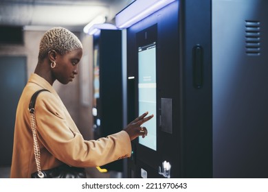 A side view of a young beautiful elegant woman with painted white very short hair paying for service underground parking or buying a subway or train ticket using an electronic self-service kiosk