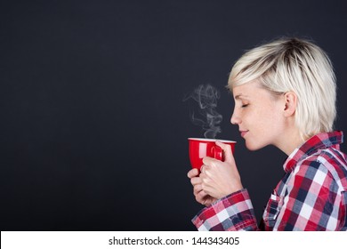 Side view of a young blond woman enjoying coffee against black background