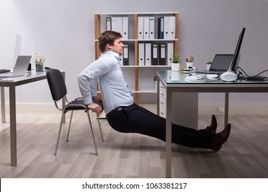 Side View Of A Young Businessman Doing Triceps Dips In Office