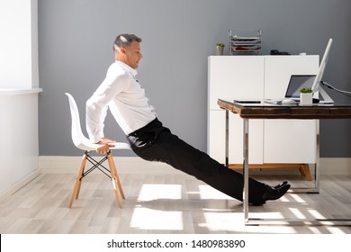 Side View Of A Young Businessman Doing Triceps Dips In Office