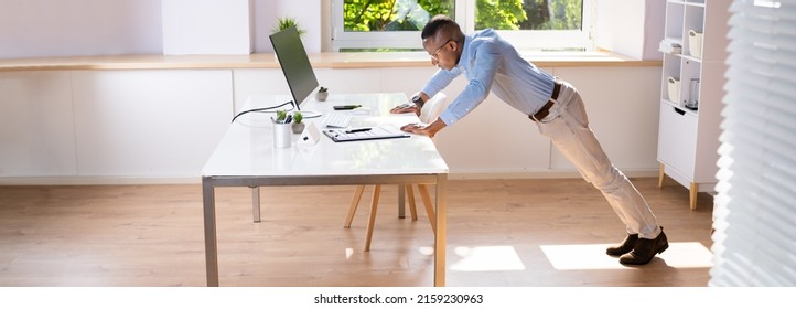 Side View Of A Young Businessman Doing Push Up On Office Desk