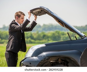 Side View Of Young Businessman Examining Broken Down Car Engine At Countryside.