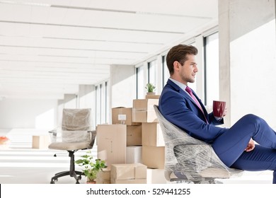 Side View Of Young Businessman Having Coffee On Chair In New Office