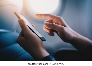 Side View Of Young Businessman Using Modern Smartphone In Aircraft, Hipster Guy Holding Mobile Device For Playing Or Working During Flight, Business Travel Concept, Flare Effect