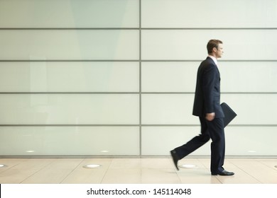 Side view of young businessman walking in passage of office - Powered by Shutterstock