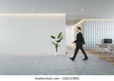 Side view of young businessman walking in modern concrete and wooden coworking office interior with empty mock up place on wall, furniture and equipment. CEO and executive concept - Shutterstock ID 2182119801